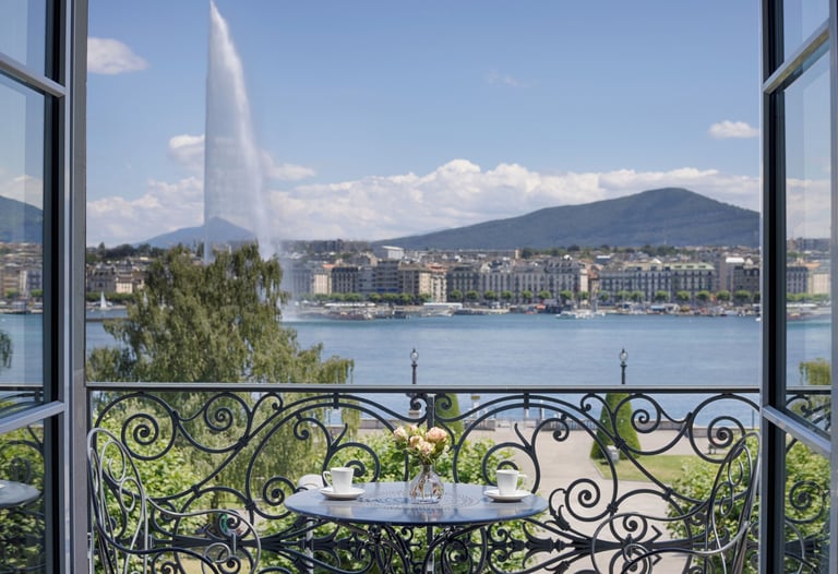 Luxury balcony view of the Jet d'Eau fountain and Lake Geneva with coffee on a bistro table.