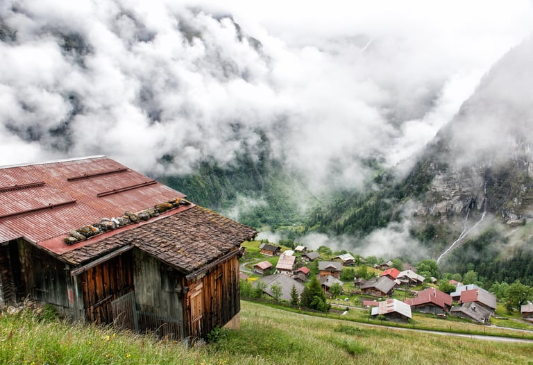 Rustic wooden chalets in a misty Swiss alpine village overlooking a foggy mountain valley.