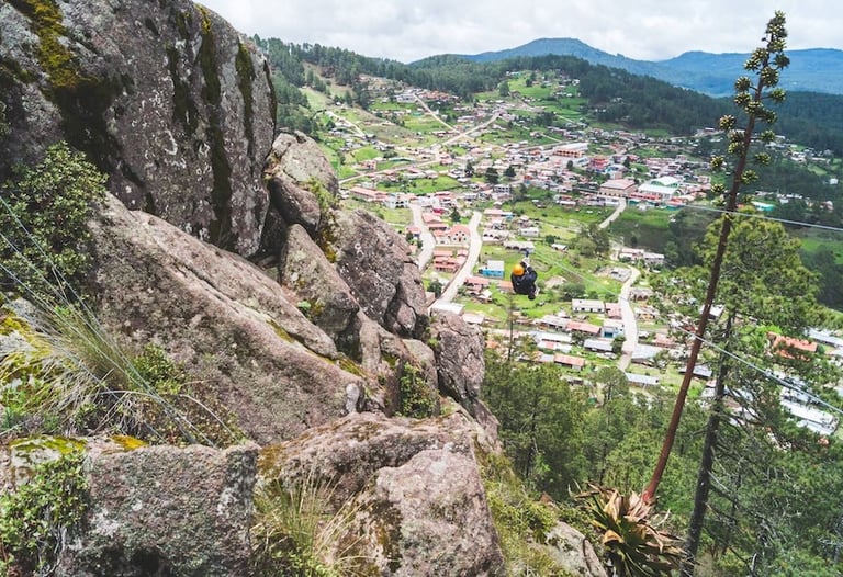 A person zip lining over a scenic mountain town surrounded by lush green pine forests.