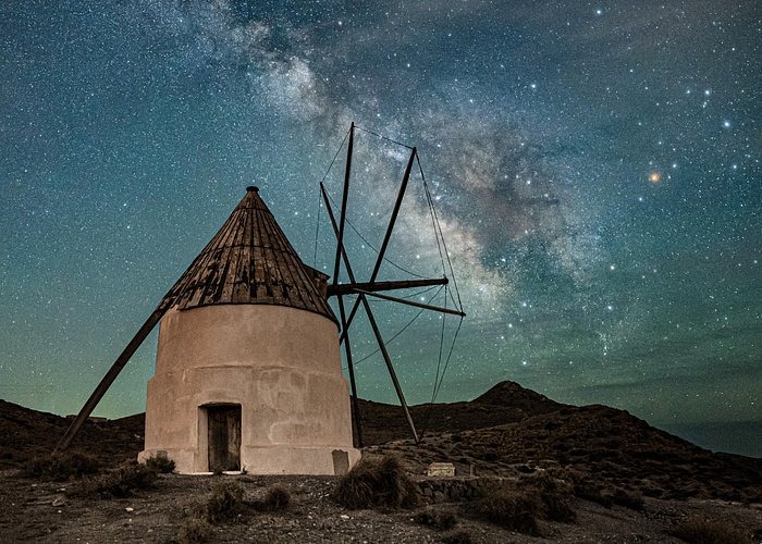 Rustic stone windmill under a vibrant Milky Way galaxy night sky in the Spanish countryside.