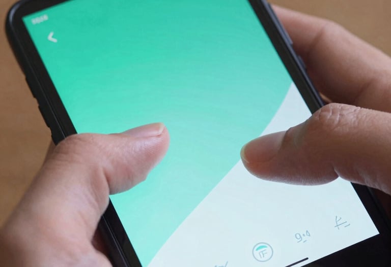 Detailed photograph of a user's thumb interacting with a beautifully designed Android interface on a handheld device. The screen displays vibrant teal and light blue gradients. North American / US setting, professional lighting.