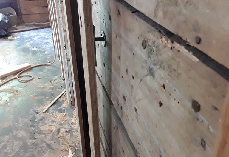 Wall reinforcement in progress with plywood panels and anchor bolts during interior renovation of an older home