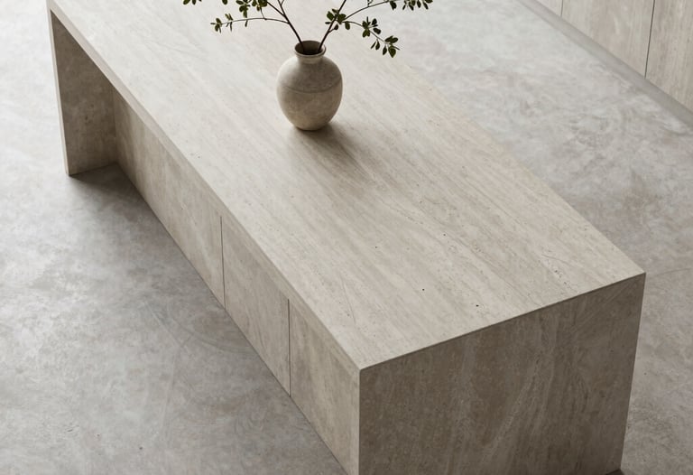 A top-down view of a minimalist kitchen island in light gray stone with a single branch in a vase. Natural daylight.