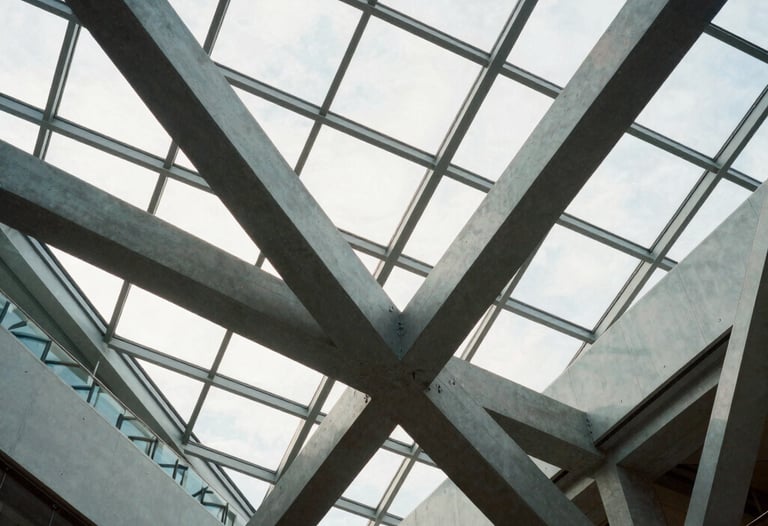 An interior shot of a modern North American atrium with complex geometric glass roofing. Structural steel beams intersect in an elegant, innovative pattern, highlighting the engineering mastery of Mazeej.