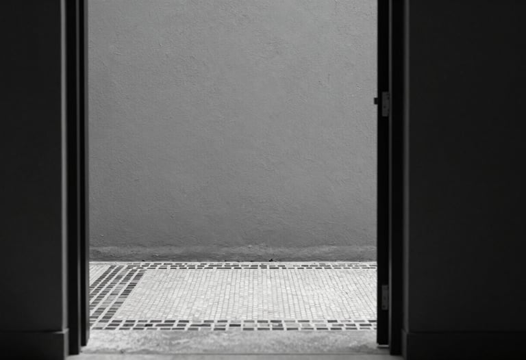 A view through a minimalist doorway showing a textured grey wall and a fragment of a monochromatic mosaic border on the floor, sharp focus, high contrast.