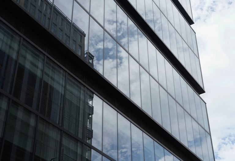 Abstract shot of modern glass architecture reflecting the sky. Sharp angles and high contrast, representing clarity and the structural nature of legal work in a contemporary Brazil.