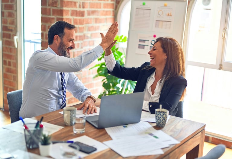 businessman and businesswoman at desk, high-fiving each other