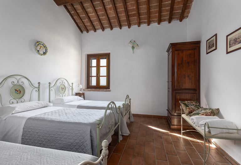 Rustic Italian bedroom with twin iron beds, terracotta tile floors, and wooden beamed ceilings.