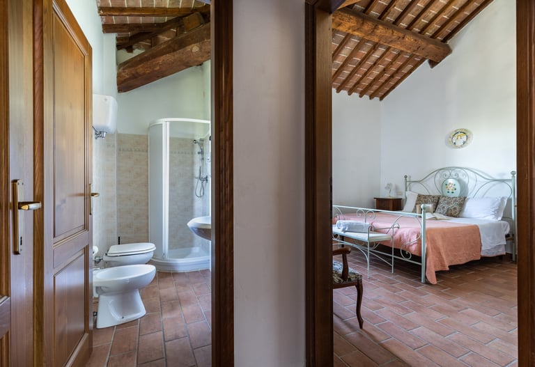 Rustic Italian bedroom and ensuite bathroom with terracotta tile floors and exposed wood beam ceilings.