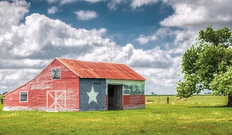 Rustic barn painted with Texas state flag motif, showcasing Texas pride in a rural Texas countryside setting