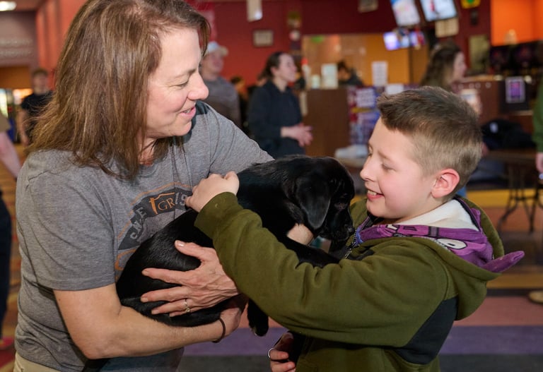a woman holding a black puppy in her arms and a boy petting it