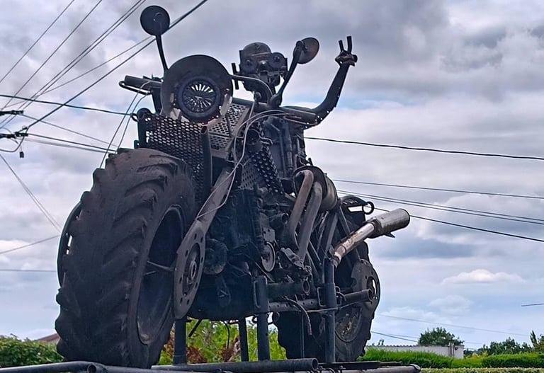 Custom-built post-apocalyptic steampunk motorcycle sculpture with large tractor tires and metal scrap parts.