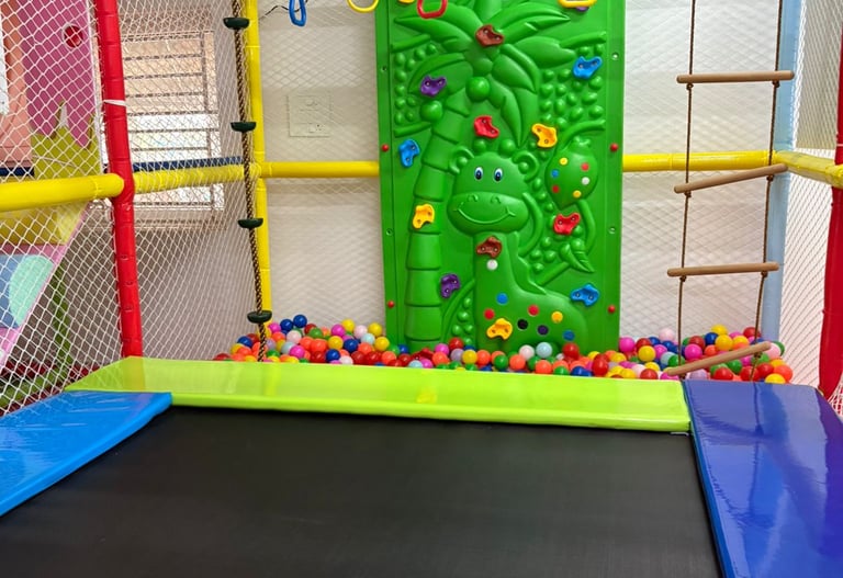 Indoor playground featuring a trampoline, ball pit, climbing wall, and hanging gym rings for kids.