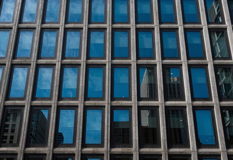 Modern urban facade with repeating geometric windows reflecting a cerulean blue sky, North American city.