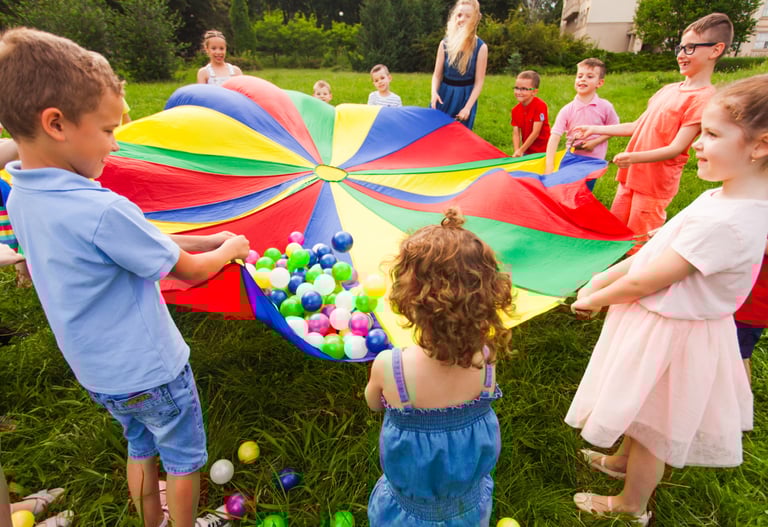 Children playing outdoors with colorful balls on a colorful blanket.