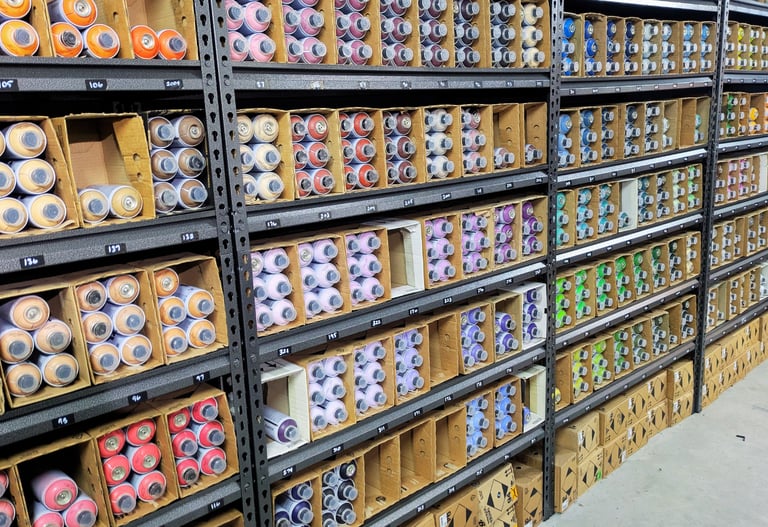 Shelves of colorful spray paint cans organized by color in HAVRE's studio.