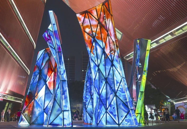 Blooming Sculpture lit up at night with its multi-colored glass panels and people walking around it