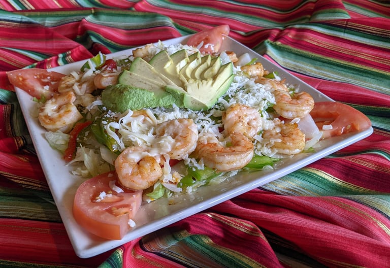 Fresh shrimp fajita salad with sliced avocado, tomatoes, and cheese on a colorful serape background.
