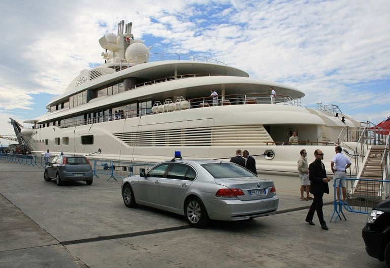 Security vehicle with flashing lights near a 130-meter luxury yacht in Italy, ensuring VIP safety.