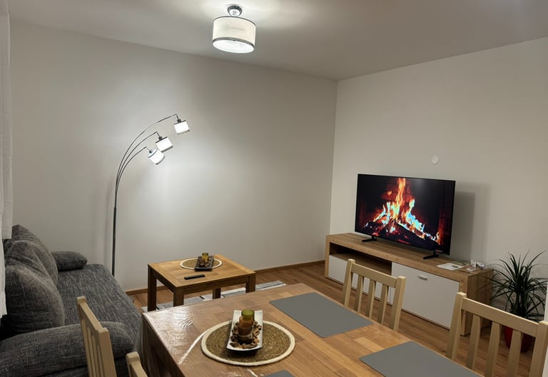 Modern living room with a fireplace video on the TV, arc floor lamp, and a wooden dining table.