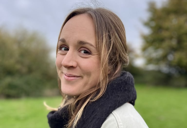A smiling blonde woman wearing a black scarf outdoors in a green field background.
