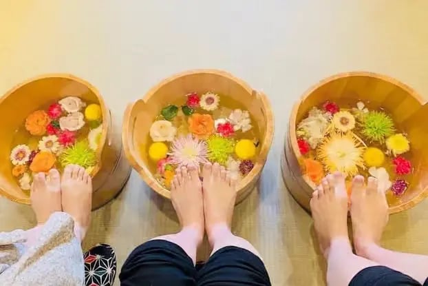 Three people soaking feet in wooden tubs filled with colorful flower petals at Kyoto spa