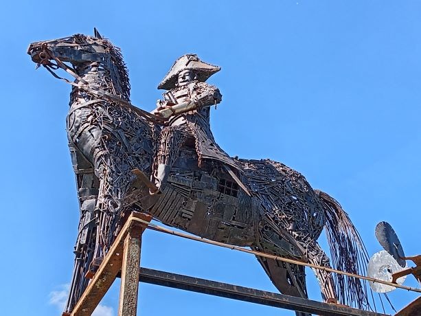 A metal scrap sculpture of an equestrian statue of Napoléon against a clear blue sky.