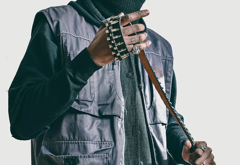 Studio photo of a man in a black jacket and a mask on, holding a belt