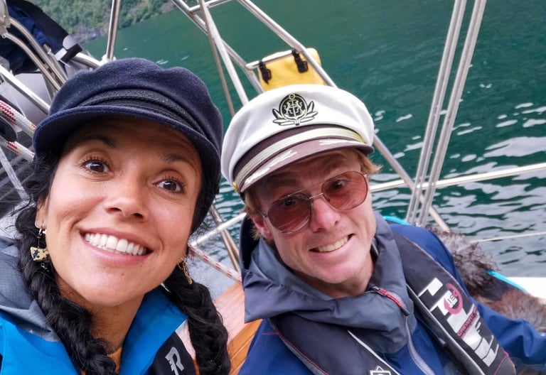 Maria og Ulrik på seilbåt i Lofoten, tett selfie om bord med sjøen i bakgrunnen.