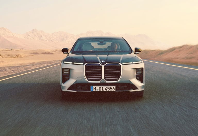 Front view of a silver BMW i7 electric luxury sedan driving on a desert road at sunset.