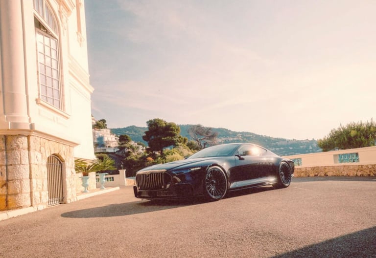 Sleek black luxury coupe parked on a sunny driveway outside a Mediterranean villa with a coastal view.