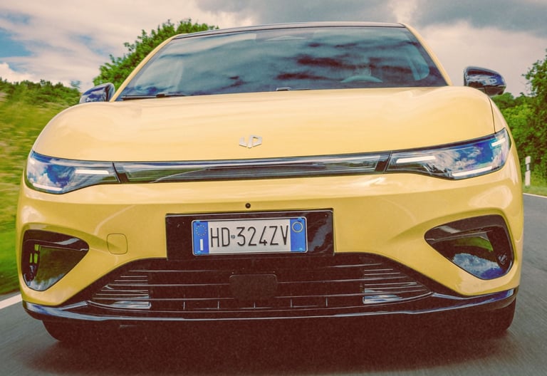 A yellow electric car driving on a scenic road with a close-up view of the front grille and headlights.