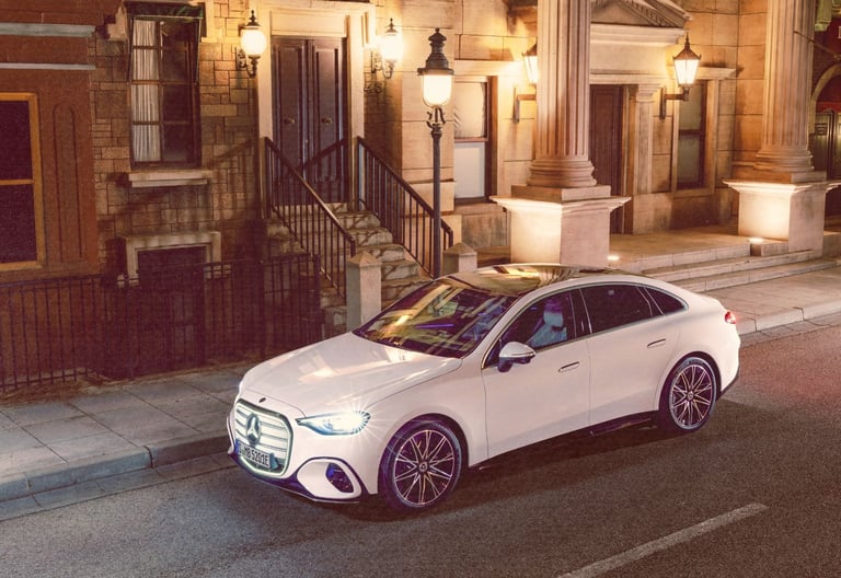 A white Mercedes-Benz electric c-class parked on a city street at night with vintage architecture.