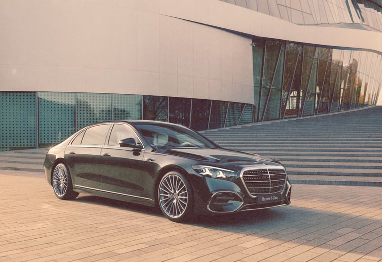 A black Mercedes-Benz S-Class luxury sedan parked in front of a modern glass building with stone steps.