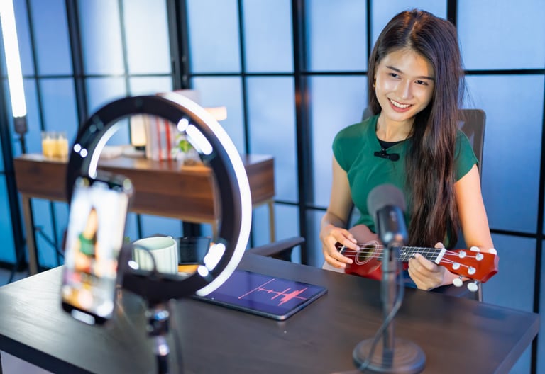 Smiling woman playing ukulele for a live stream with a ring light and smartphone.