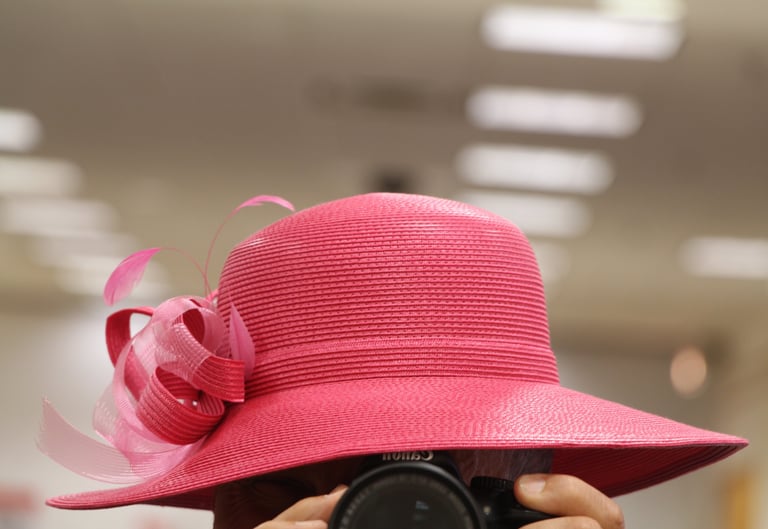Male figure holding a photo camera and wearing red women's straw hat.