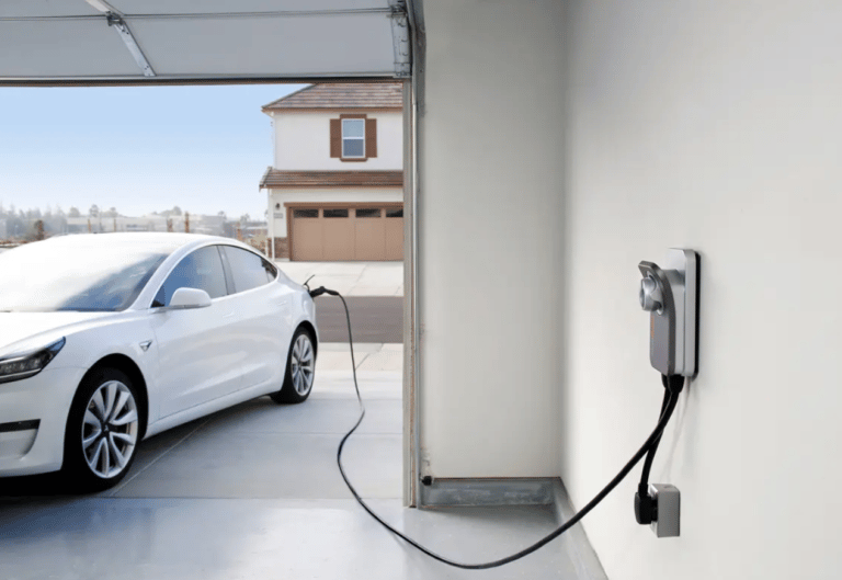 White Tesla electric car charging in a residential garage using a wall-mounted EV home charger.