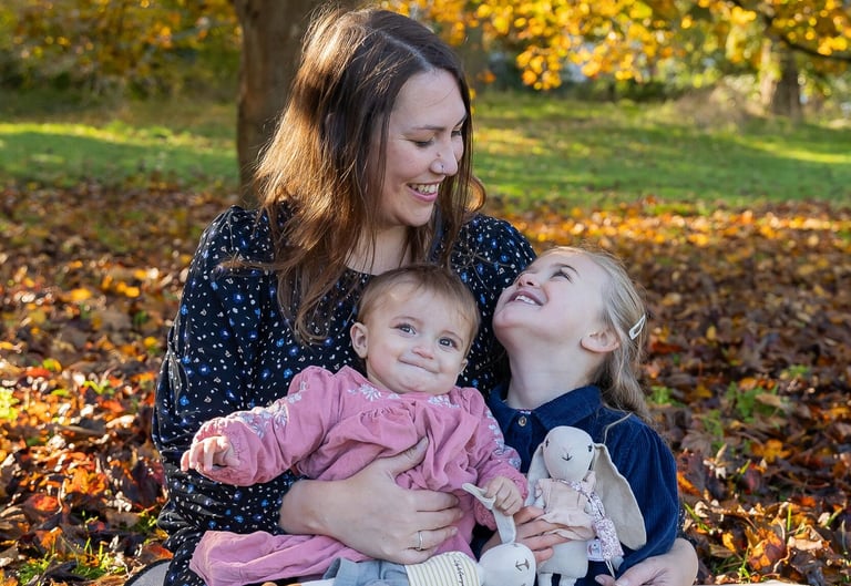 a woman sitting on a blanket with two children smiling towards the older girl who looks back smiling