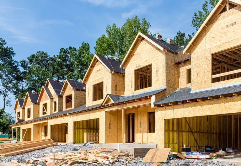 Row of townhomes under construction showing wood framing and OSB sheathing at an active job site.