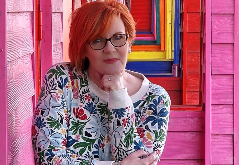 Dawn Vincent Celebrant smiling leaning on brightly coloured beach huts