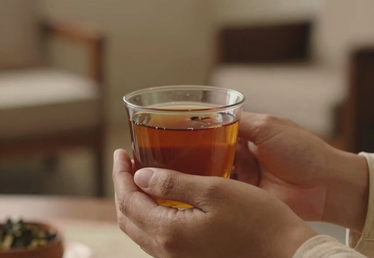 A peaceful close-up of hands holding a warm cup of herbal tea in a serene consulting room in India. Soft focus, warm organic sandalwood colors, comforting and calming mood, Global South Asian / Indian setting.