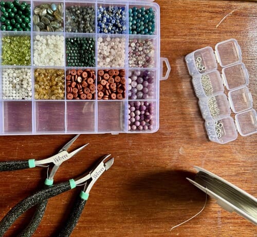 Materiales para la elaboración de joyería, cuentas organizadas en una caja, pinzas y alambre.