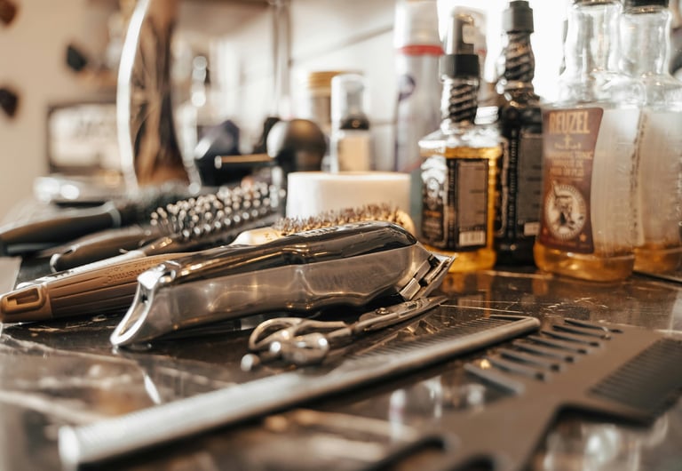 Barber tools including electric clippers, combs, and Reuzel hair tonic on a salon counter.