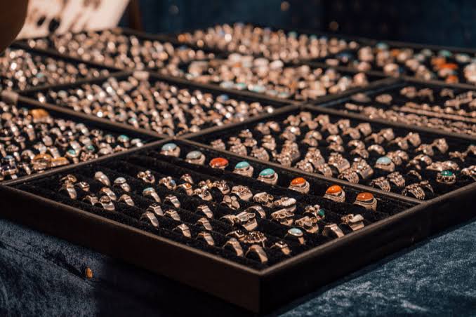 Collection of handmade silver rings with turquoise and amber gemstones displayed in jewelry trays.
