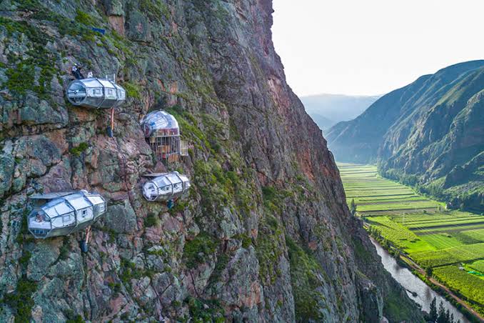 Transparent luxury glass capsules hanging on a cliffside in Peru's Sacred Valley overlooking a river.