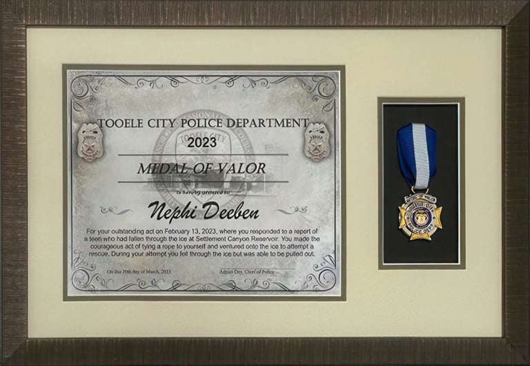 Framed Tooele City Police Department Medal of Valor certificate and blue ribbon award for Nephi Deeben.