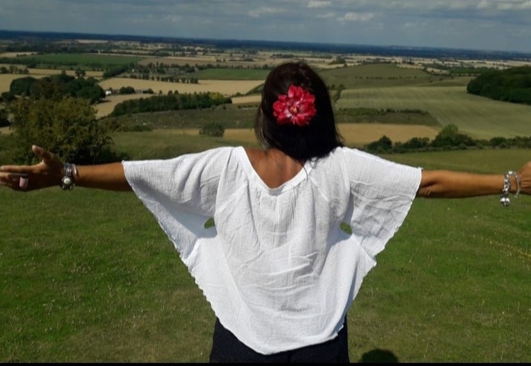 An image of the back of Sheila Cristina on the top of a hill. In front of her is a beautiful view of many fields in England.