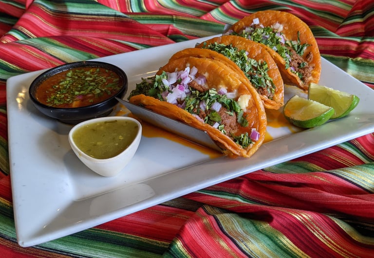 Plate of authentic Mexican beef birria tacos with cilantro, onions, lime, and dipping consomme.