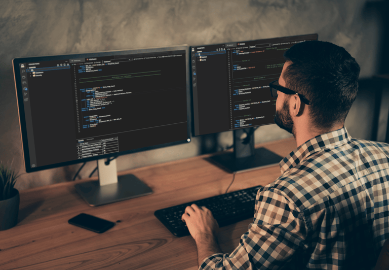 A man sitting at a desk with two monitors and a keyboard writing code