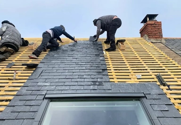 Trois couvreurs posant des ardoises sur charpente de toiture avec Velux